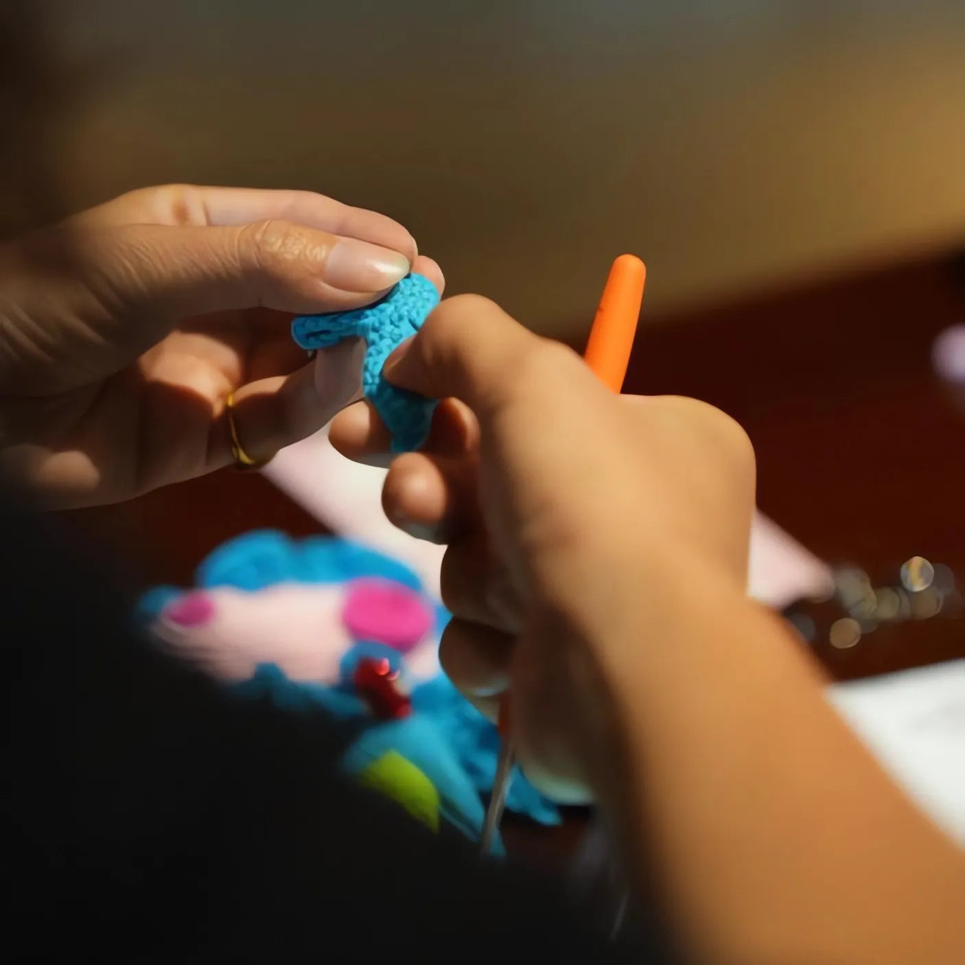 Close-up of hands crocheting a small blue fabric item with a blurred background