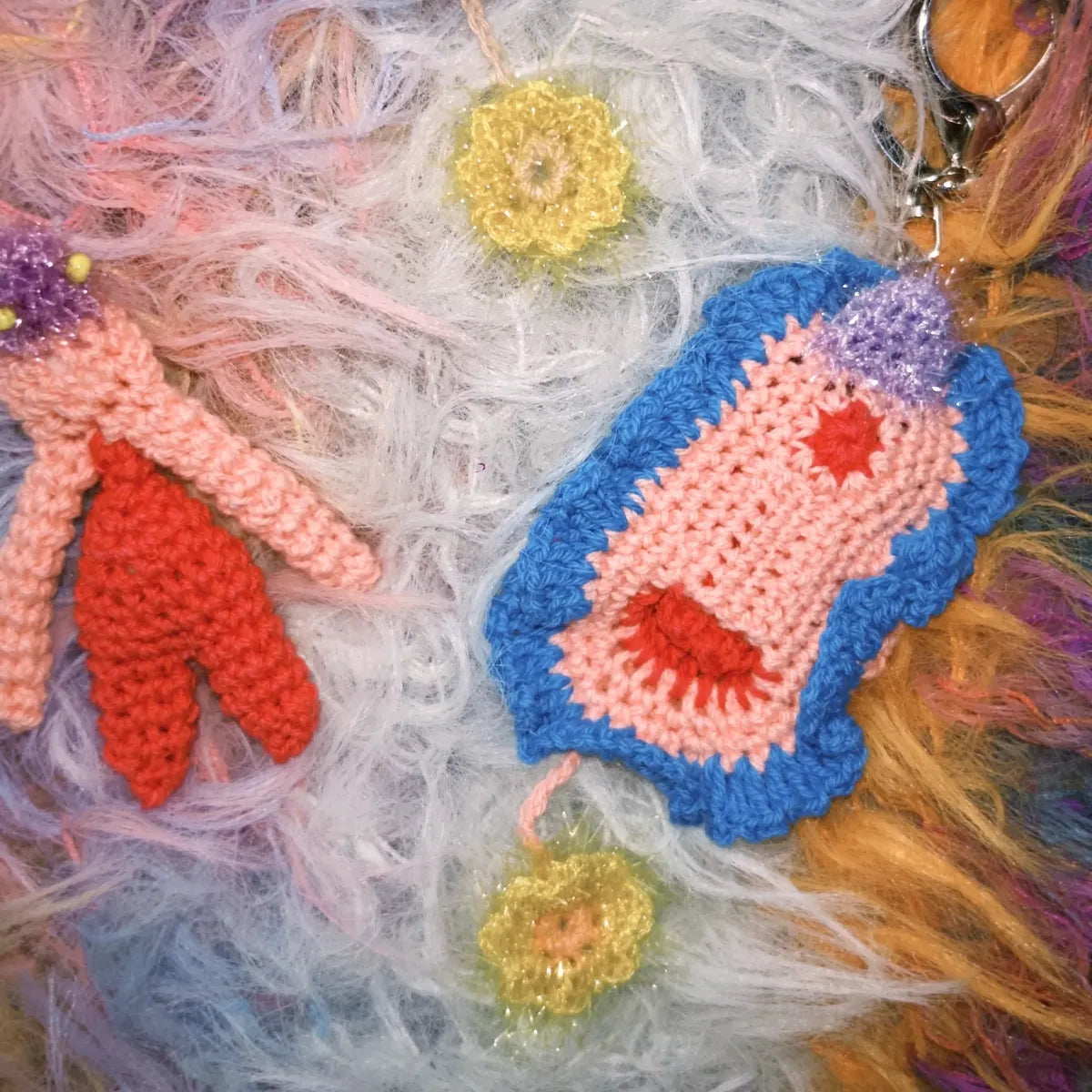 Colorful crocheted clitoral keychain with yarn strands in the background